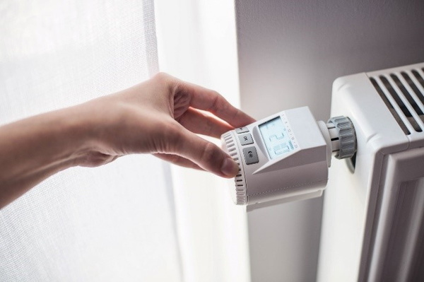Eine Hand dreht am Thermostat einer Heizung und stellt diese auf 21° Celcius