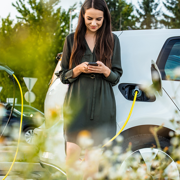 Frau an Smartphone neben E-PKW Ladestation