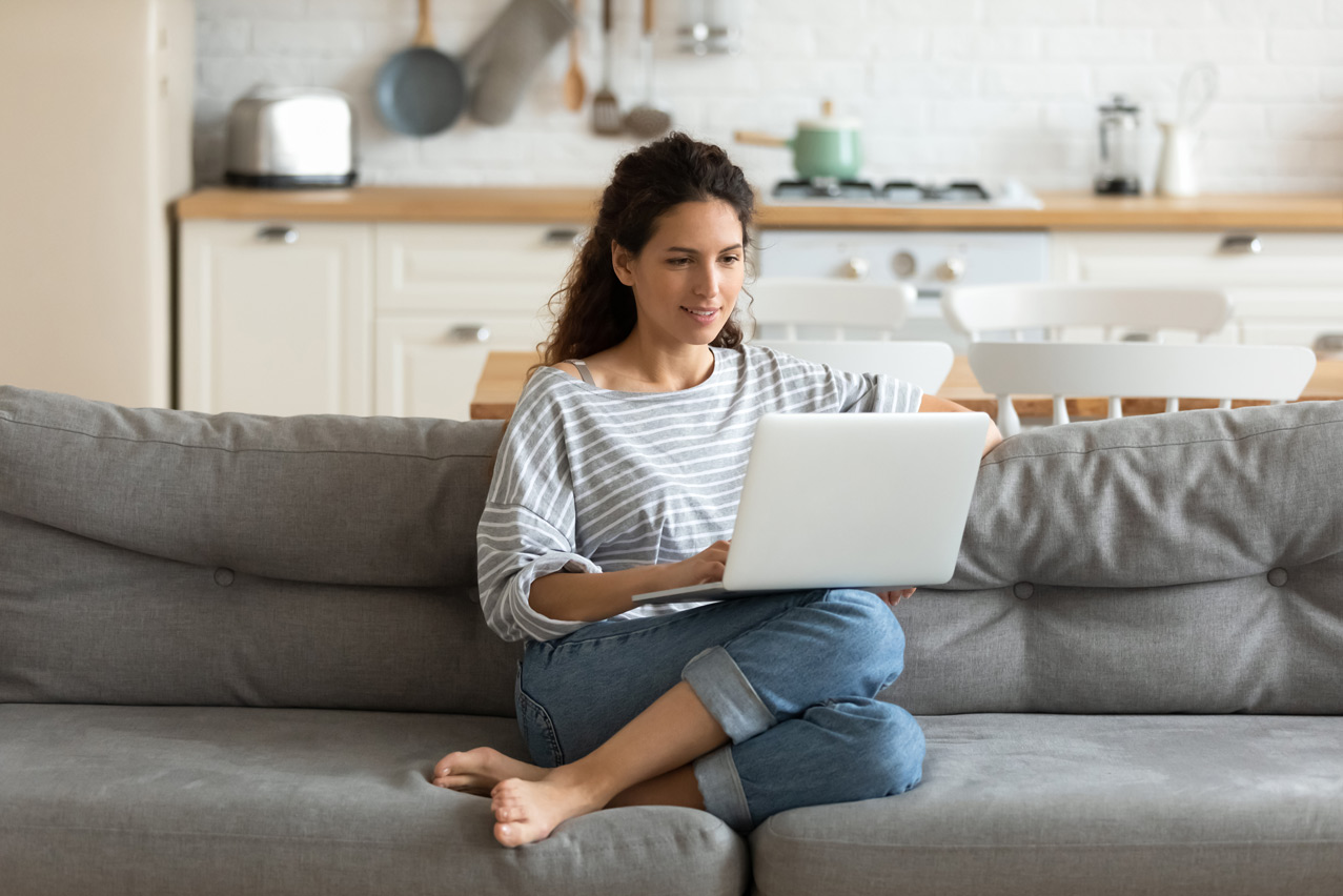 Frau sitzt auf Couch mit Laptop