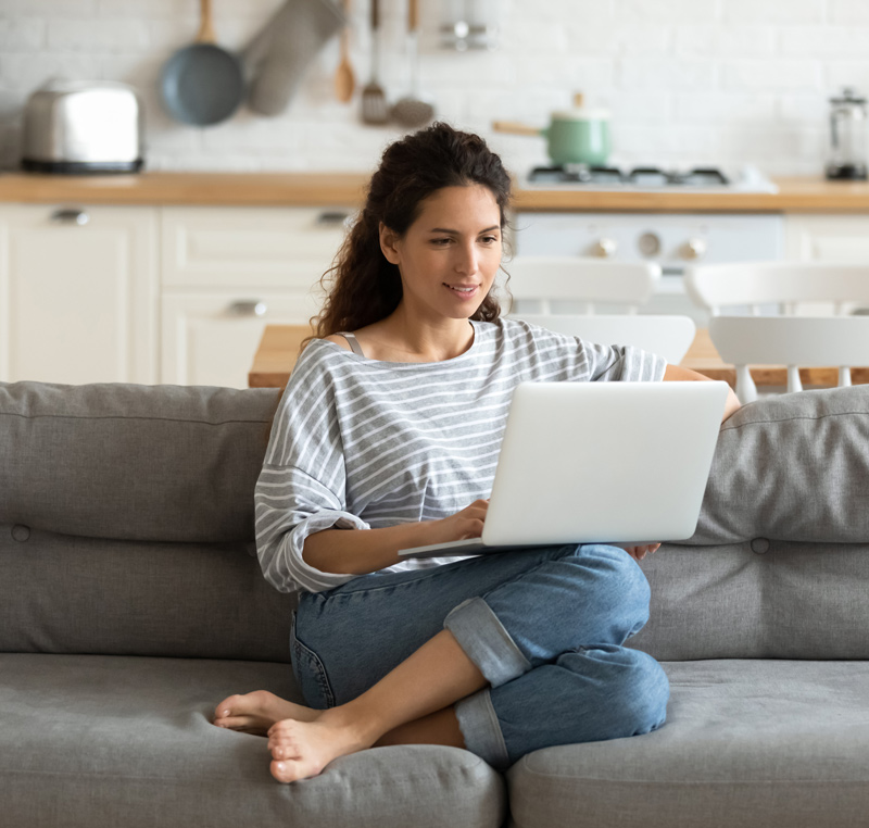 Frau sitzt auf Couch mit Laptop